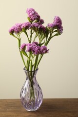 Beautiful flowers in glass vase on wooden table against beige background, closeup
