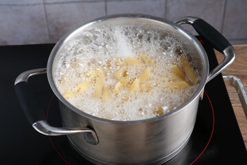 Fresh pasta boiling in pot with water on electric stove, closeup