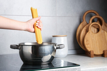 Woman putting tagliatelle pasta into pot on electric stove in kitchen, closeup