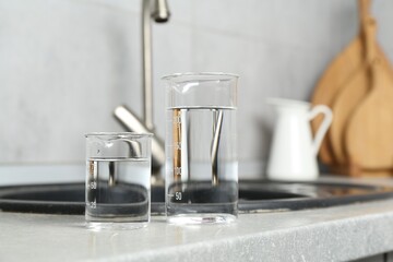 Beakers with clean water near sink on counter in kitchen, closeup