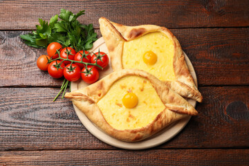 Tasty khachapuris with cheese, eggs, tomatoes and parsley on wooden table, flat lay