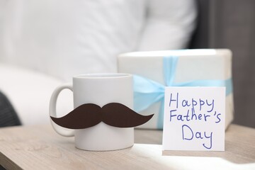 Happy Father's Day card, cup with mustache and gift on wooden table at home, closeup