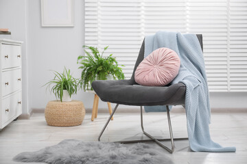 Comfortable grey armchair with pink pillow and blanket in living room. Interior design