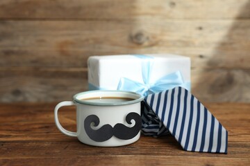 Happy Father's Day. Cup with mustache, tie and gift on wooden table