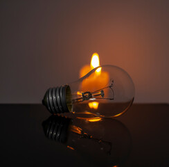 Burning candle near a switched off light bulb in complete darkness. Blackout, electricity off, energy crisis or power outage, concept image