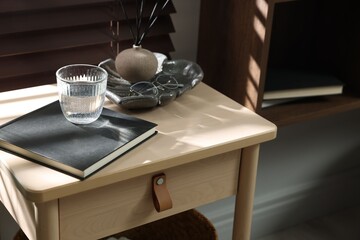 Wooden side table with glass of water, notebook and air reed diffuser indoors