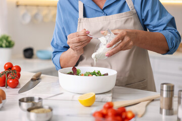 Senior woman cooking salad at white marble table in kitchen, closeup