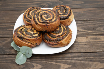 Close-up of spiral poppy seed rolls on wooden table. Homemade pastry dessert with rich filling, arranged on a plate with leaves. Perfect for bakery promotion, cafe menus, food blogs, and recipe ideas