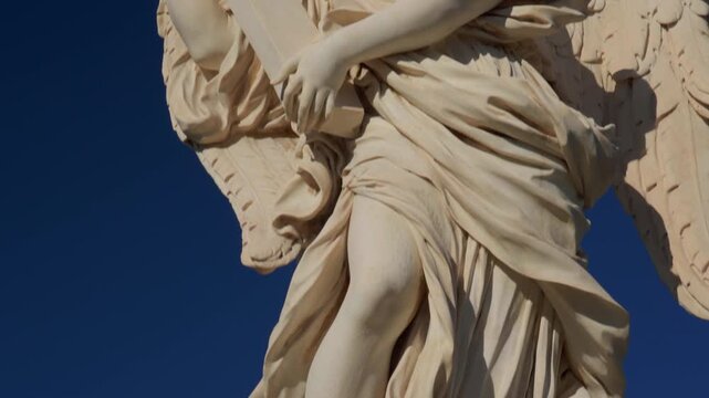 Angel statue holding cross on Ponte Sant&rsquo;Angelo, baroque marble sculpture with dramatic pose against deep blue sky in Rome