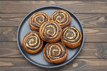Close-up of homemade poppy seed rolls on a plate over wooden table. Golden brown pastry swirls filled with rich poppy seed filling. Concept of homemade baking, sweet pastry, desserts and bakery food