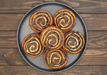 Close-up of homemade poppy seed rolls on a plate over wooden table. Golden brown pastry swirls filled with rich poppy seed filling. Concept of homemade baking, sweet pastry, desserts and bakery food