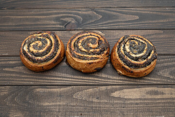Homemade poppy seed rolls on rustic wooden background. Golden crust with sweet spiral filling, fresh baked pastry, perfect for breakfast or tea time. Traditional European dessert on a white plate.