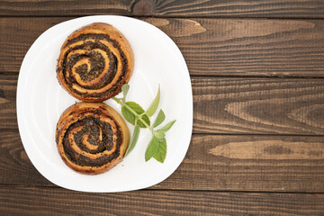 Close-up of spiral poppy seed rolls on wooden table. Homemade pastry dessert with rich filling, arranged on a plate with leaves. Perfect for bakery promotion, cafe menus, food blogs, and recipe ideas