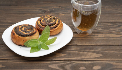 Close-up of spiral poppy seed rolls on a rustic wooden table. Homemade pastry dessert with rich filling, arranged on a plate with leaves. Perfect for bakery promotion, cafe menus, food blogs