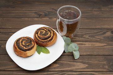 Close-up of spiral poppy seed rolls on a rustic wooden table. Homemade pastry dessert with rich filling, arranged on a plate with leaves. Perfect for bakery promotion, cafe menus, food blogs
