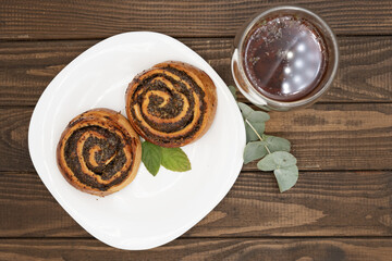 Close-up of spiral poppy seed rolls on a rustic wooden table. Homemade pastry dessert with rich filling, arranged on a plate with leaves. Perfect for bakery promotion, cafe menus, food blogs