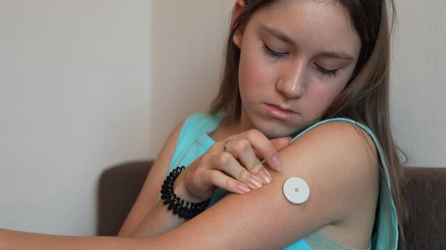 Caucasian Girl with diabetes checking blood glucose level at home using continuous glucose monitor. The girl checks the glucose level