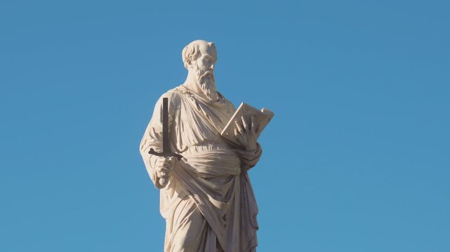 Marble statue of Saint Paul holding sword and book against clear blue sky, symbol of Christian faith and apostolic authority in Rome