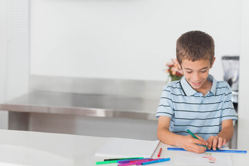 Naklejka premium Boy drawing on white paper at kitchen counter with scattered markers and blue ruler, copy space