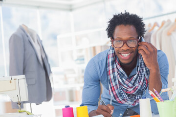 Fashion designer sketching on worktable via smartphone with sewing machine in studio