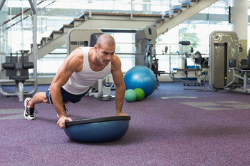 Man performing balancing push-up on Bosu ball on purple gym carpet with weight machines, copy space