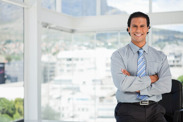 Fototapeta premium Mid adult Hispanic man leaning on black chair with Bluetooth earpiece at office windows, copy space
