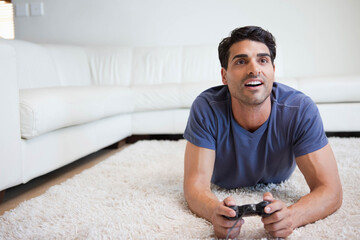 Mid adult man lying in living room on white shag rug holding black controller, copy space