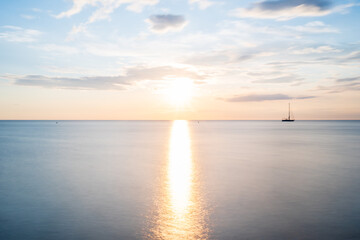 Obraz premium Langzeitbelichtung bei Sonnenuntergang am Meer mit Boot am Horizont