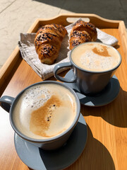 Traditional Italian breakfast. Fresh croissants and cappuccino on a wooden tray. European food and pastry. Morning meal and cozy home breakfast. Coffee break.