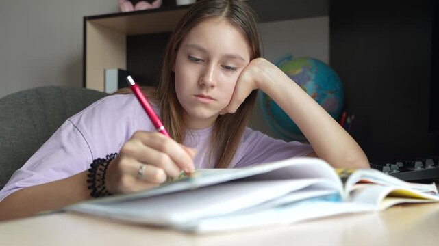 girl studying at home. A girl in a blouse gets bored while doing homework. A female student is tired in class. A schoolgirl solves a difficult example while sitting at a table.