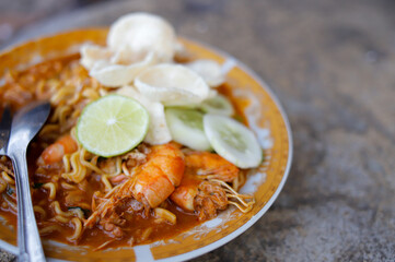 Spicy stir-fried shrimp instant noodles seafood on white plate on stone, close-up with copy space