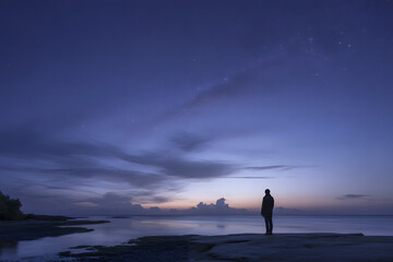 Solitary figure silhouetted against a dramatic twilight sky over calm water