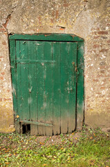 Obraz premium Old damaged green wooden door in a weathered wall with padlock and chain