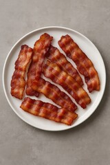 Crispy fried bacon strips served on white plate top view of savory breakfast food