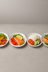 Assorted healthy meals with grilled chicken salmon potatoes rice and fresh vegetables served on white plates top view