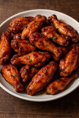 Plate of spicy glazed chicken wings served on wooden table, close up view of delicious crispy appetizer with sauce