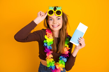 Joyful woman celebrating summer vibes in colorful lei with travel tickets against a vibrant yellow...