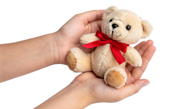 Cute little teddy bear with red bow held gently in soft hands a heartwarming symbol of comfort and affection