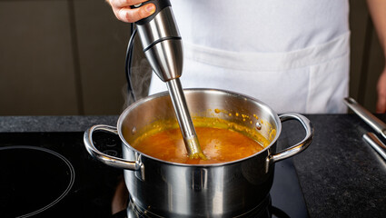 A person blending soup with an immersion blender