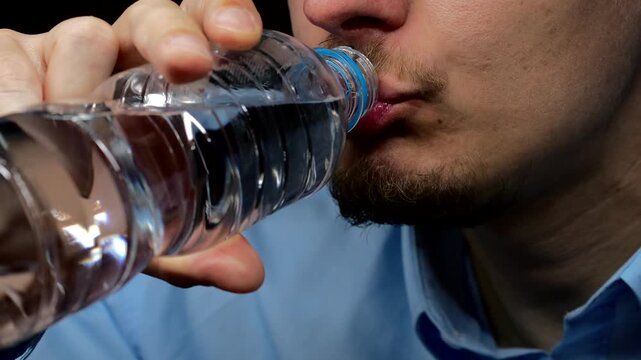Mouth of an adult swallowing water from a plastic container.
The man maintains the body's water balance and drinks a lot of water.
Healthy lifestyle and bottled water