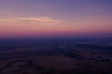 Aerial drone view of village and river at dawn with purple pink sunrise sky over fields and forests