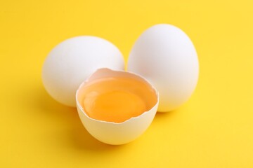 Whole and broken chicken eggs on yellow background, closeup
