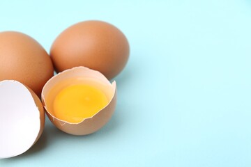 Whole and broken chicken eggs on light blue background, closeup. Space for text