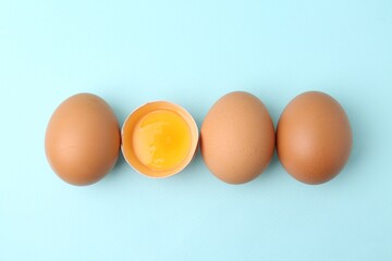 Whole and broken chicken eggs on light blue background, top view