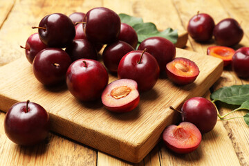 Whole, cut cherry plums and board on wooden table, closeup