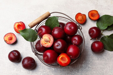 Ripe cherry plums, green leaves and metal basket on grey textured table, flat lay