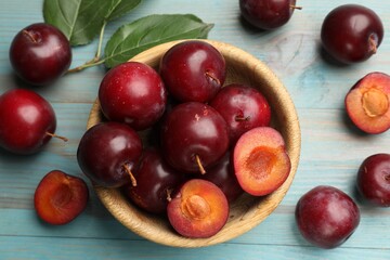 Ripe cherry plums, bowl and green leaves on light blue wooden table, flat lay