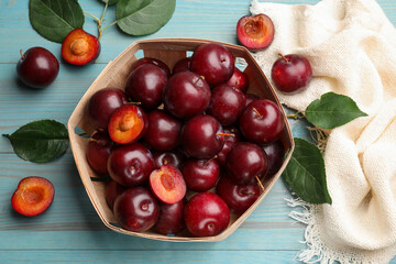 Whole, cut cherry plums, cloth and green leaves on light blue wooden table, flat lay