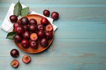 Ripe cherry plums, cloth and green leaves on light blue wooden table, flat lay. Space for text