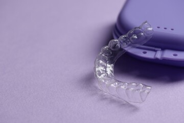 One clear aligner and retainer case on violet background, closeup. Space for text